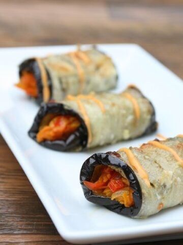 Baked eggplant rollups stuffed with vegetables and topped with garlic aioli.