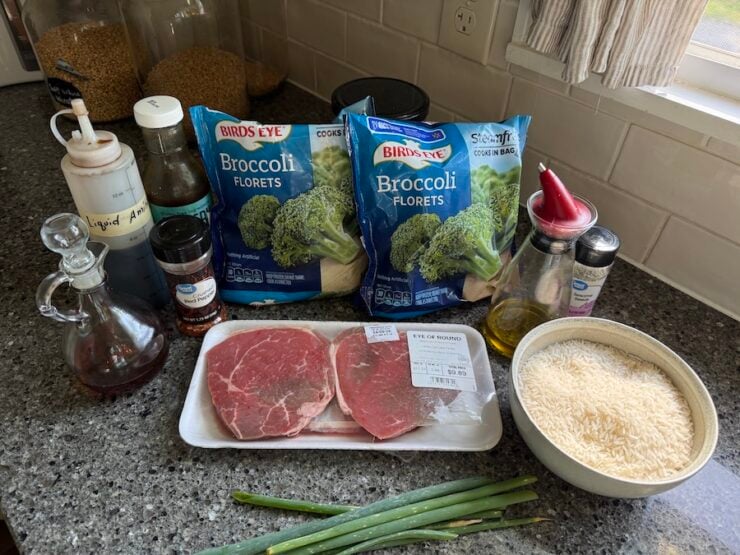 image of all the ingredients for beef and broccoli (eye of round steak), frozen broccoli florets, oil, white sesame seeds, soy-free stir fry sauce, coconut liquid Aminos, red pepper flakes, and green onions.