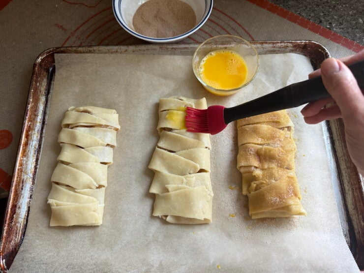 image of brushing egg wash on the braided apple hand pies and covered with a cinnamon sugar topping