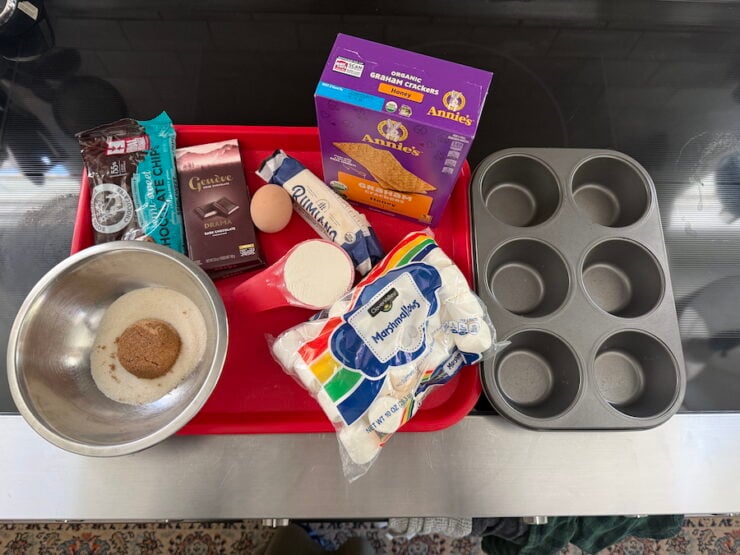 image of all the ingredients for S'mores tarts and a jumbo muffin pan (ingredients are: graham crackers, marshmallows, butter, egg, all-purpose flour, chocolate, sugar, baking soda, and salt).