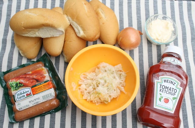 ingredients for bratwurst sandwiches (bread rolls, sauerkraut with carrots, raw onions, mayonnaise, ketchup, smoked bratwursts).