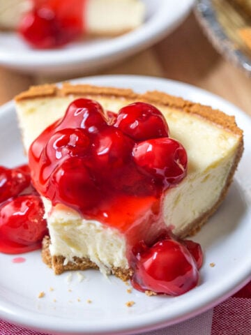 a slice of cheesecake with cherry pie filling over the top on a white plate