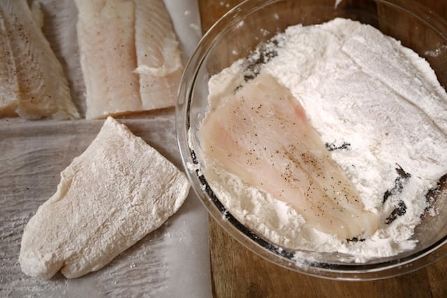 Swai fillets being dredged in all-purpose flour for an even coating.