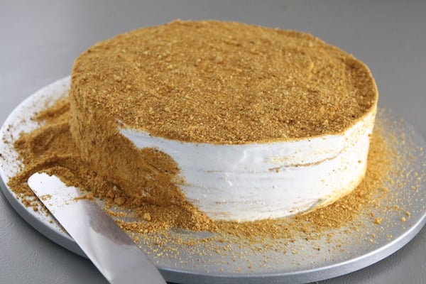 Russian honey cake being assembled on a cake plate with crumbs