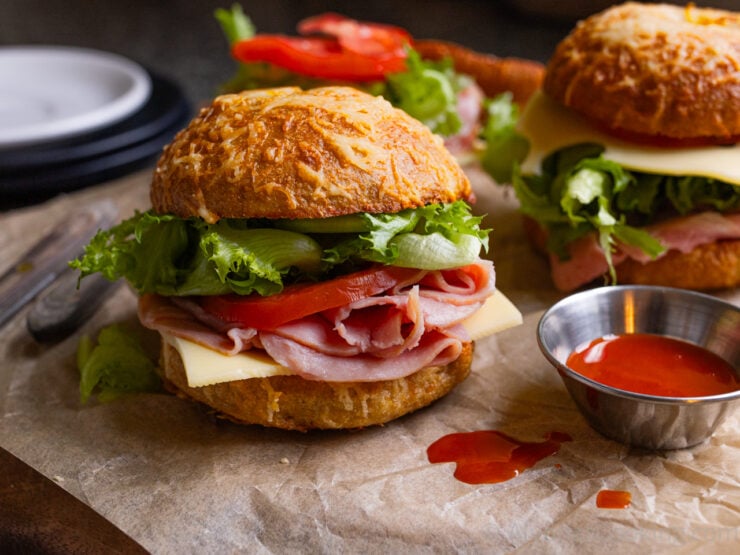 image of asiago bagel sandwiches photographed on parchment paper with hot sauce
