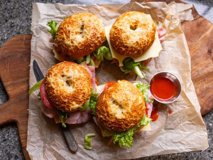 image of four asiago bagel sandwiches photographed with hot sauce on a cutting board lined with brown parchment paper