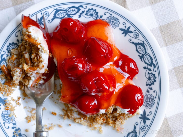 a close-up image of a cheesecake pretzel dessert topped with canned cherry pie filling