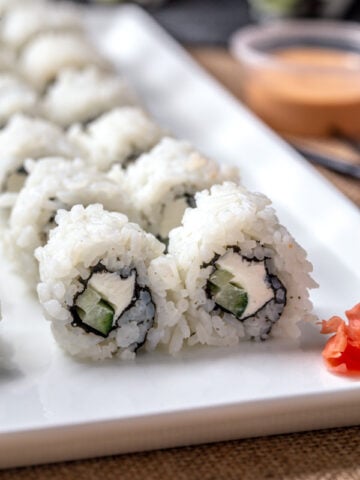 Philadelphia sushi roll on white plate with spicy mayo and ginger