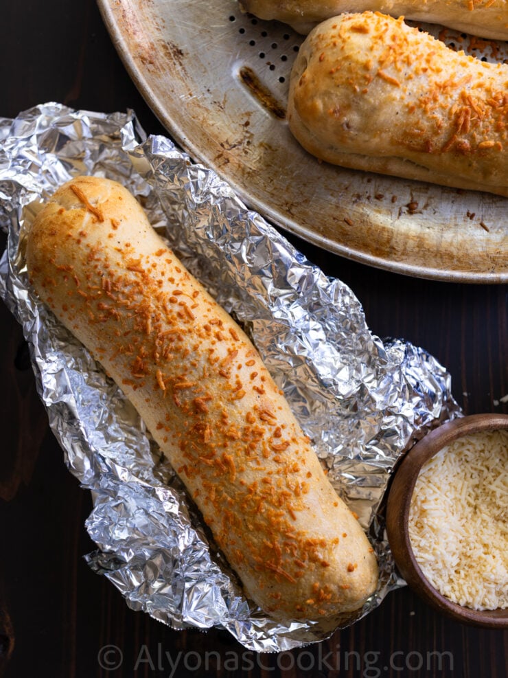 image of a homemade Costco Chicken Bake wrapped in foil placed by a pizza pan of chicken bakes