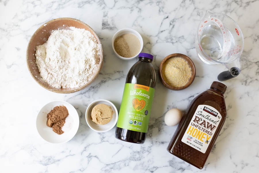 All ingredients for Outback bread (whole wheat flour, bread flour, brown sugar, blackstrap, molasses, cocoa powder, salt, dry active yeast, water, granulated sugar, honey, egg, and cornmeal). 