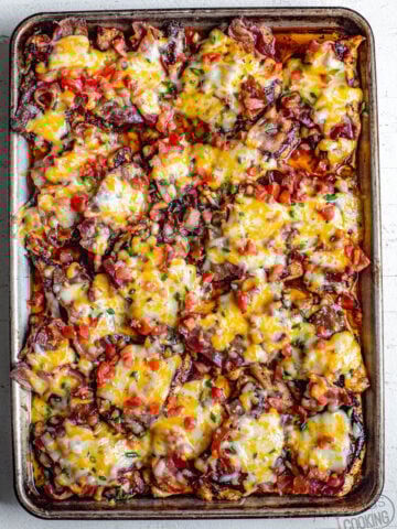 cheesy bacon BBQ chicken on a baking sheet baked from the oven. This Monterey chicken is a Chilis inspired dish topped with bbq sauce, bacon, Monterey Jack cheese, and tomatoes