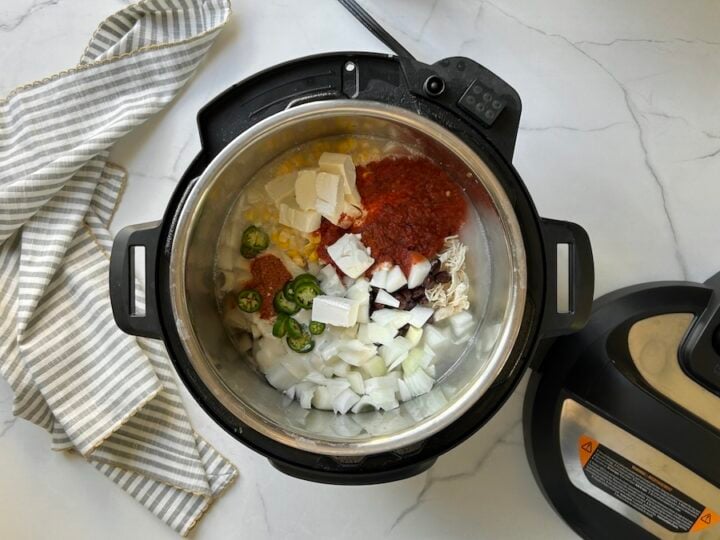 all of the white chicken chili ingredients in the Instant Pot (corn, beans, chili powder, cayenne pepper, salsa, cream cheese, ranch, and heavy cream)