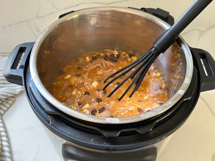 Cooked white chicken chili in the Instant Pot with a whisk to remove lumps