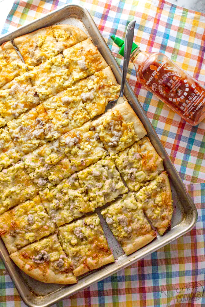 best breakfast pizza recipe on a greased sheet-pan topped with sausage gravy sauce, cheese, and scrambled eggs!
