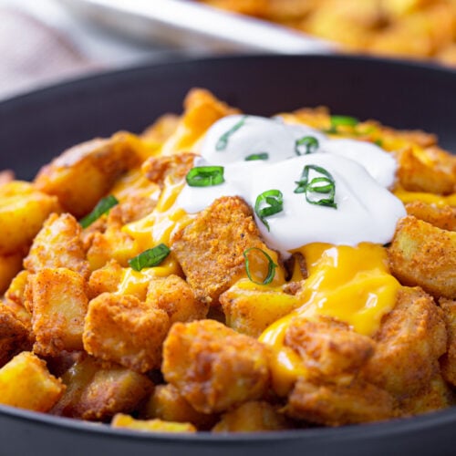 taco bell cheesy fiesta potatoes with sour cream and cheese on a black plate and green onions
