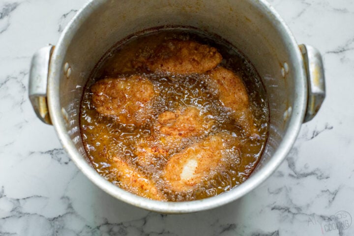 homemade crispy chicken being fried in a large pot with soybean oil