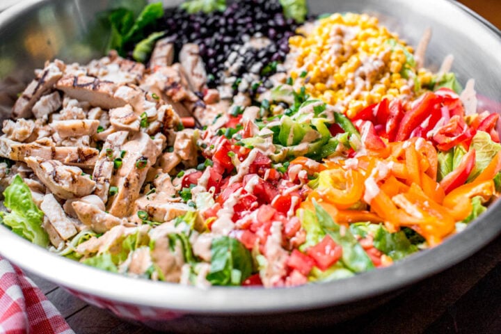 how to make southwest salad in a large mixing bowl with black beans, corn, grilled chicken, bell peppers, tomatoes, chipotle ranch dressing, and romaine lettuce
