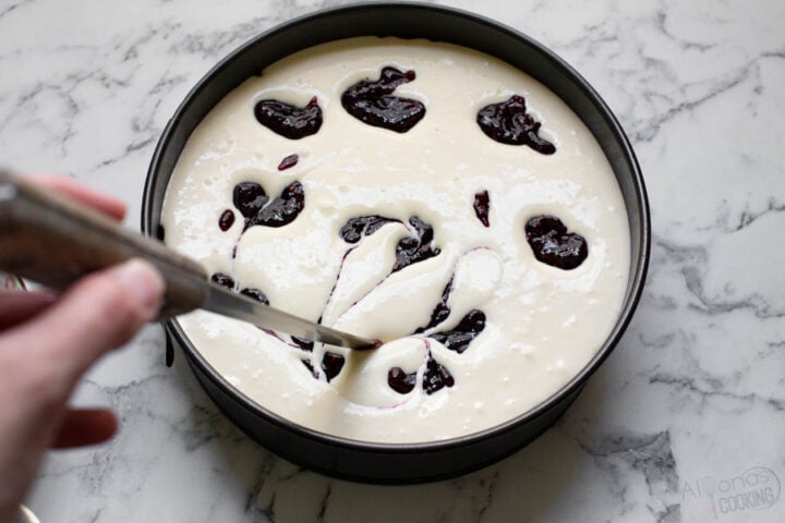 how to make a raspberry swirl cheesecake running a knife through raspberry preserves to make swirls