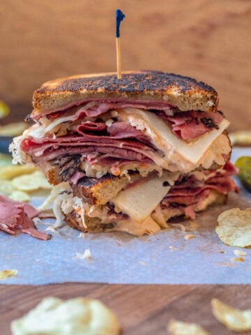 Reuben Sandwich cut in half and stacked on top of each other then served with potato chips and pickles