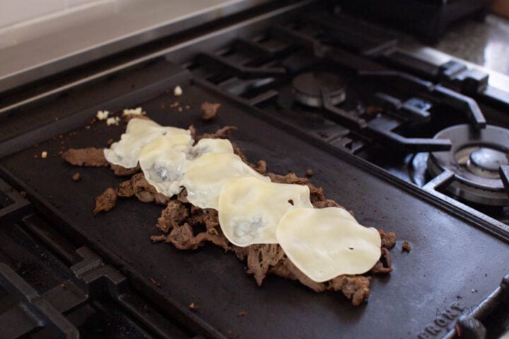 image of provolone cheese melting on top of cooked beef shavings on a hot griddle for Philly Cheesesteaks