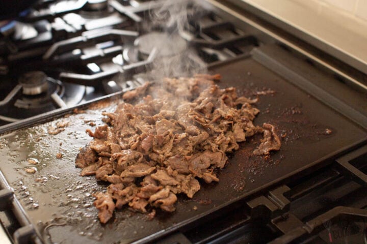 image of cooked beef shavings on a hot griddle for Philly Cheesesteaks