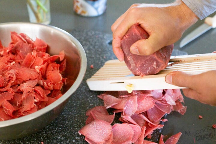 image of partially frozen beef being thinly sliced on a Mandoline slicer