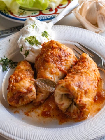 moms stuffed cabbage rolls on a plate filled and rolled with rice and meat then garnished with sour cream and dill
