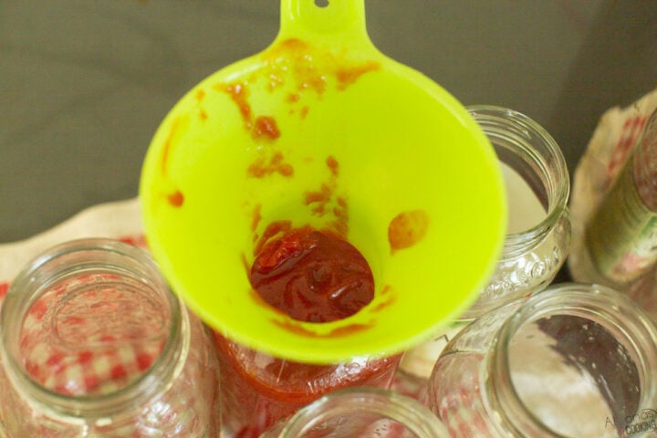pouring tomato ketchup in a canning jar through a funnel