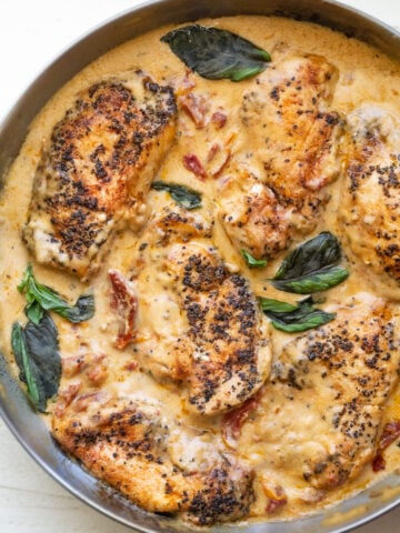 tuscan chicken (creamy sun-dried tomato chicken) in a skillet with fresh basil
