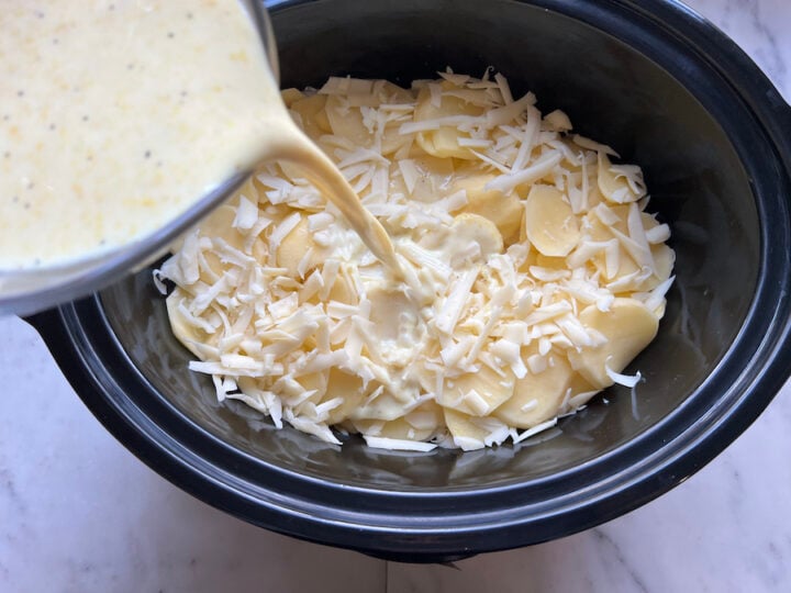 pouring the milk mixture over the layers of scalloped potatoes