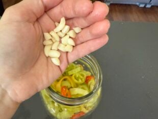 Adding garlic to a jar of sliced banana peppers