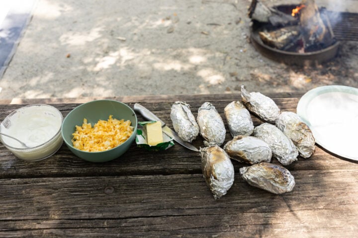 image of serving campfire baked potatoes on a picnic table outdoors