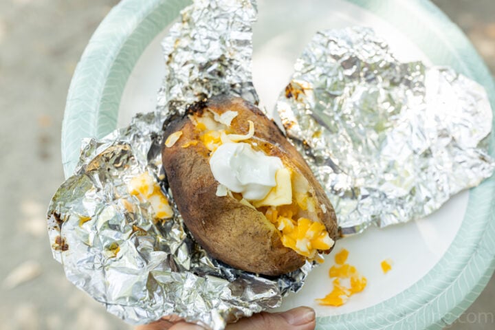 image of a baked potato cooked over a fire on a paper plate unwrapped from foil
