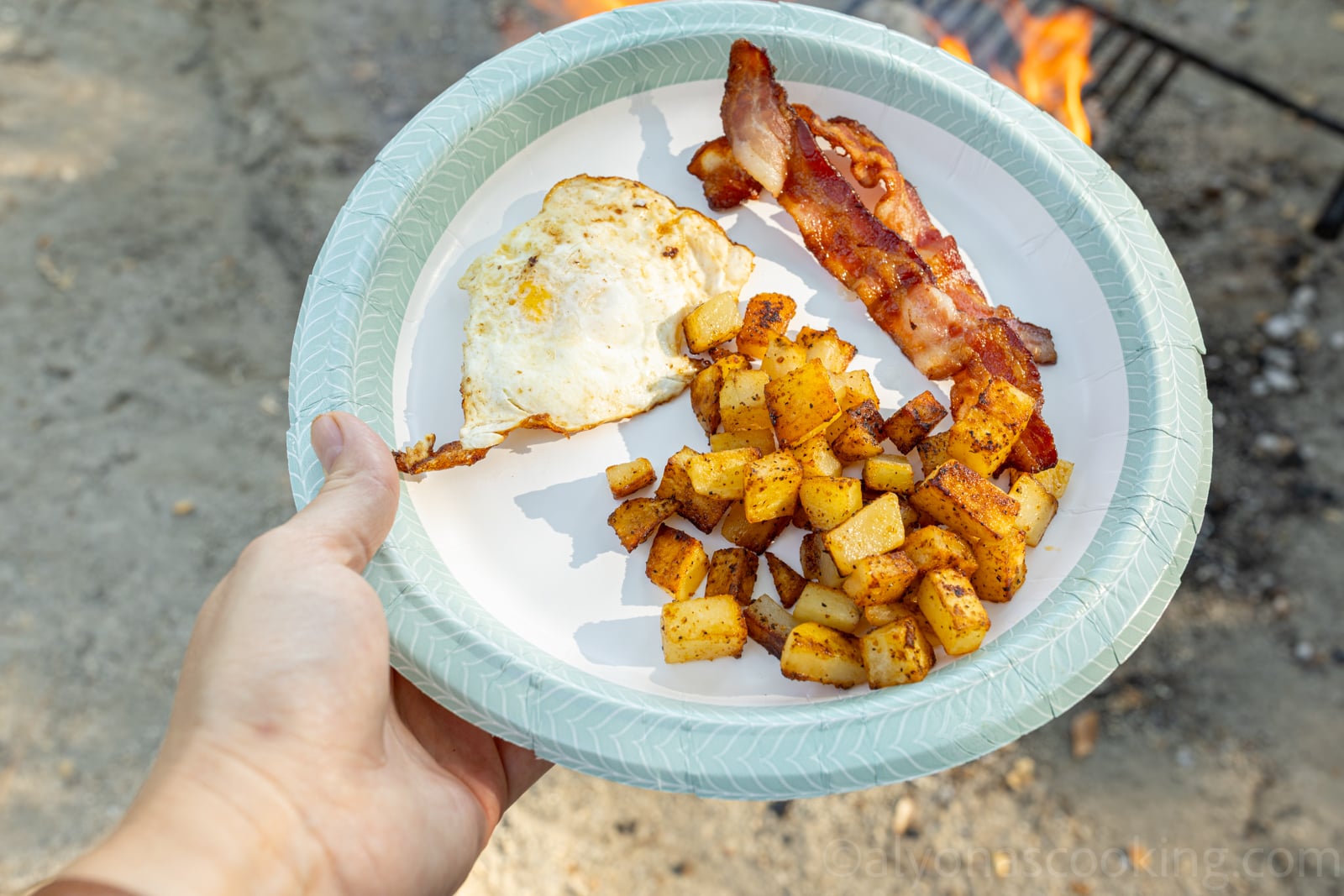 image of camping breakfast potatoes served with fried eggs and fried bacon on a disposable plate