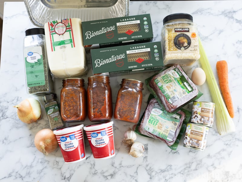 image of all ingredients and equipment for homemade freezer lasagna (lasagna noodles, homemade pasta sauce, ricotta cheese, vegetables, ground beef seasonings, and Italian cheeses.