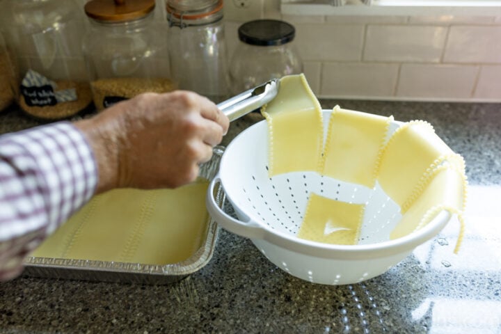 image o soaked uncooked lasagna noodles being placed on a colander for freezer lasagna recipe