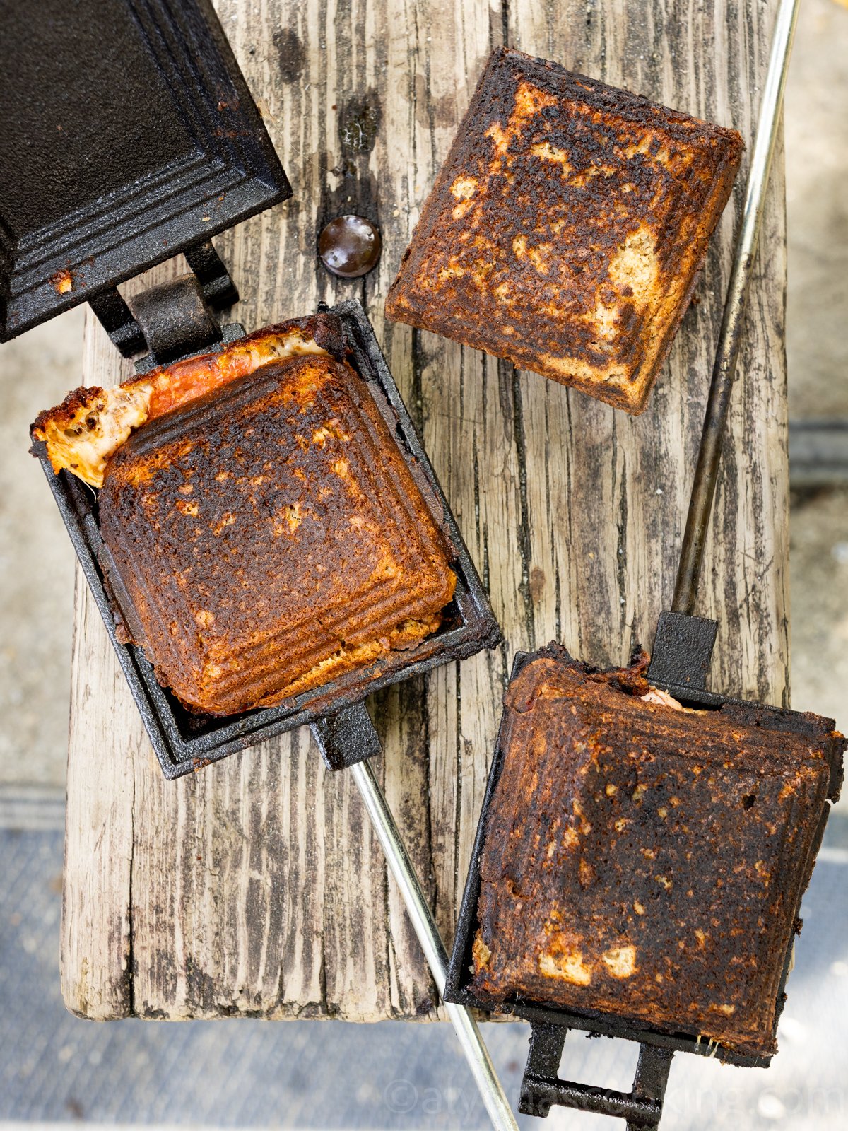 Image of Mountain pies in a mountain pie maker on a picnic table (pizza sandwich, ham and cheese sandwich, and breakfast ham, egg, and cheese sandwich)