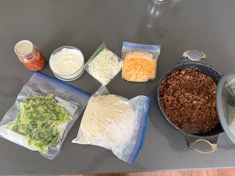 image of chopped veggies, homemade biscuit dough, taco meat, grated cheese, sour cream, pico de Gallo all prepped for woof em sticks (camping)