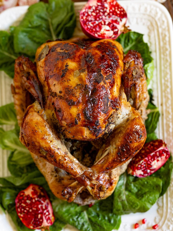 image of a roasted Thanksgiving turkey on a serving platter garnished with pomegranates and green leafy lettuce