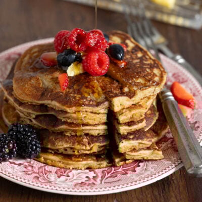 image of whole grain einkorn pancakes on a red vintage plate with berries and maple syrup
