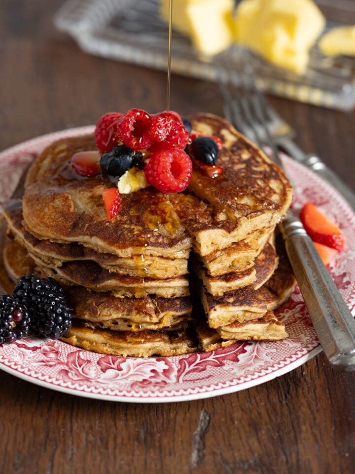 image of whole grain einkorn pancakes on a red vintage plate with berries and maple syrup