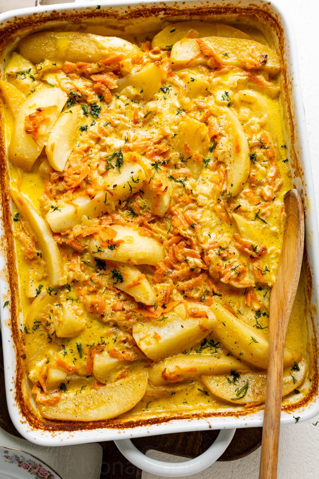 creamy baked potato wedges in heavy cream, carrots, and onions sprinkled with dill in a casserole dish