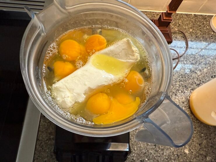 image of two dozen eggs in a blender with a pack of cream cheese ready to be blended for sheet pan eggs