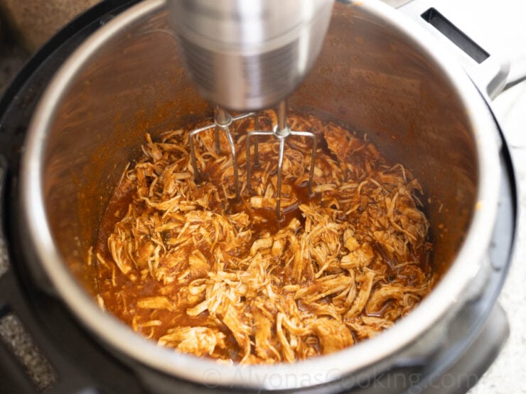Image of shredding the Instant Pot chicken enchiladas with a hand mixer
