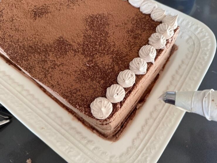 image of adding final touches to a homemade tiramisu cake (piping out swirls on the dusted cocoa powder)