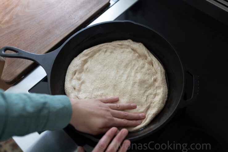 image of Alyona stretching out the whole wheat sourdough pizza dough in a cast-iron pan.