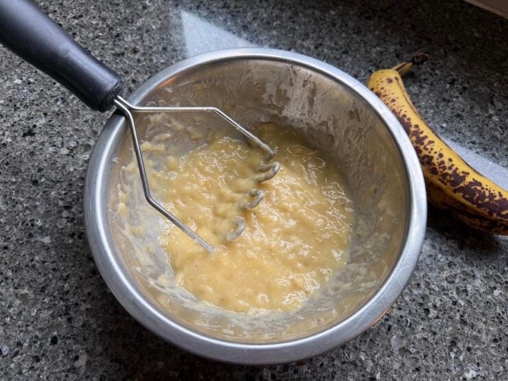 image of mashed ripe bananas shown with a potato masher to make a fine paste