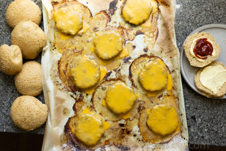 image of oven baked burgers on a sheet pan with melted cheese and hamburger buns on the side