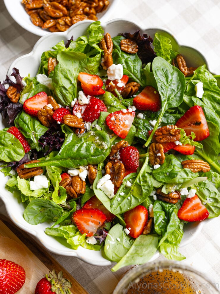 strawberry spinach salad plated on a scalloped plate and topped with candied pecans, sliced strawberries, feta, and sweet onion poppy seed dressing.