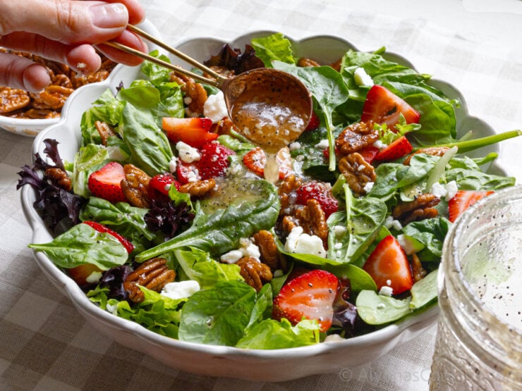 image of assembled strawberry spinach salad in a bowl drizzled with poppy seed dressing
